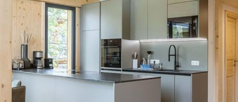A modern kitchen with grey cabinets, a central island, and a large window providing natural light.