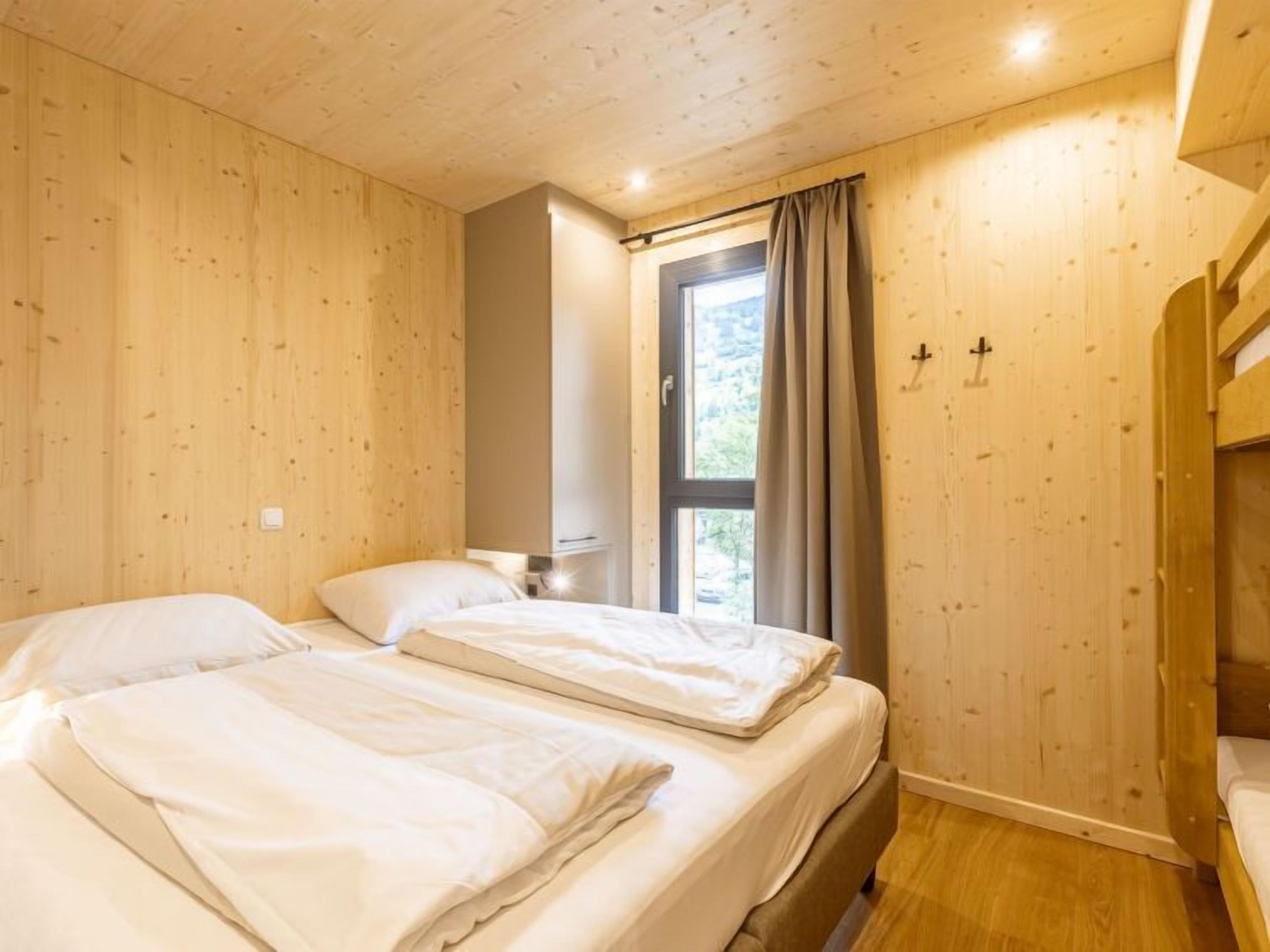 Habitación con paredes de madera y un gran ventanal con cortinas. Hay dos camas con ropa de cama blanca.