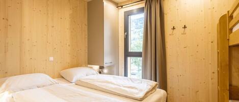 Habitación con paredes de madera y un gran ventanal con cortinas. Hay dos camas con ropa de cama blanca.