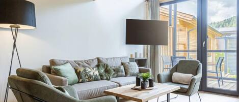 Una sala de estar moderna con un sofá, dos sillones, una mesa de centro y un amplio ventanal con vistas a una cabaña de madera.