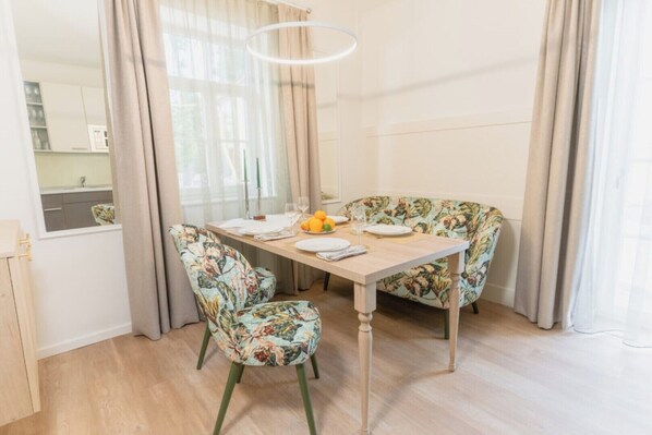 Ein Essbereich mit einem Holztisch, floral gepolsterten Stühlen, einer Obstschale und einer modernen Pendelleuchte.