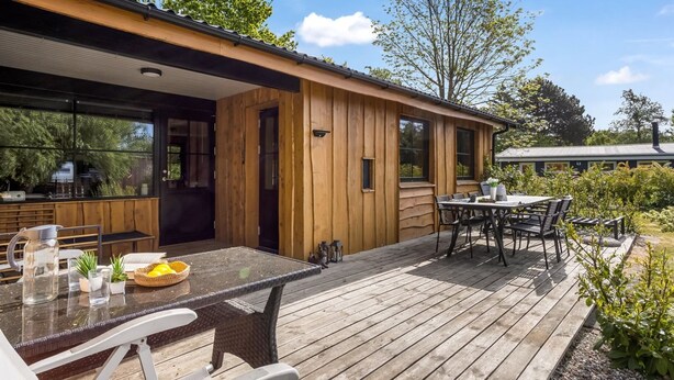 Una cabaña de madera con un porche, asientos exteriores y un amplio ventanal con vistas a un jardín.