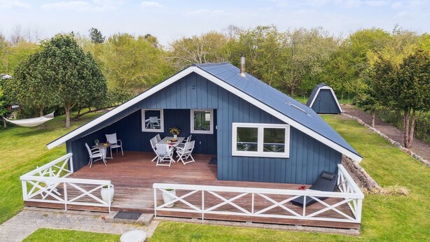 En blå hytte med en træterrasse, hvide gelændere og et spiseområde med stole og et bord.