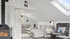 En moderne stue i loftstil med pejs, sofaarrangement, en lænestol og et ovenlys.