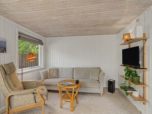 Un cuarto acogedor con sofá, sillón y una pequeña mesa. Hay un televisor en un estante y una ventana con vistas a la vegetación.