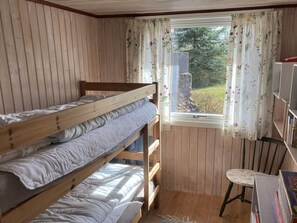 A room with a bunk bed, a window with floral curtains, a chair, and a bookshelf.