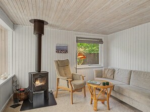 Una habitación acogedora con una estufa de leña, un sillón cómodo, un sofá y una mesita.