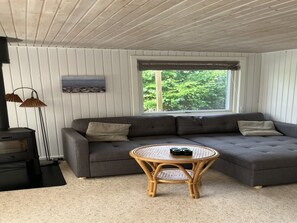 A living room with a sectional sofa, a round wicker coffee table, a fireplace, and a window with a view of greenery. - "Kaarina" - 550m from the sea by Interhome (Rødby)
