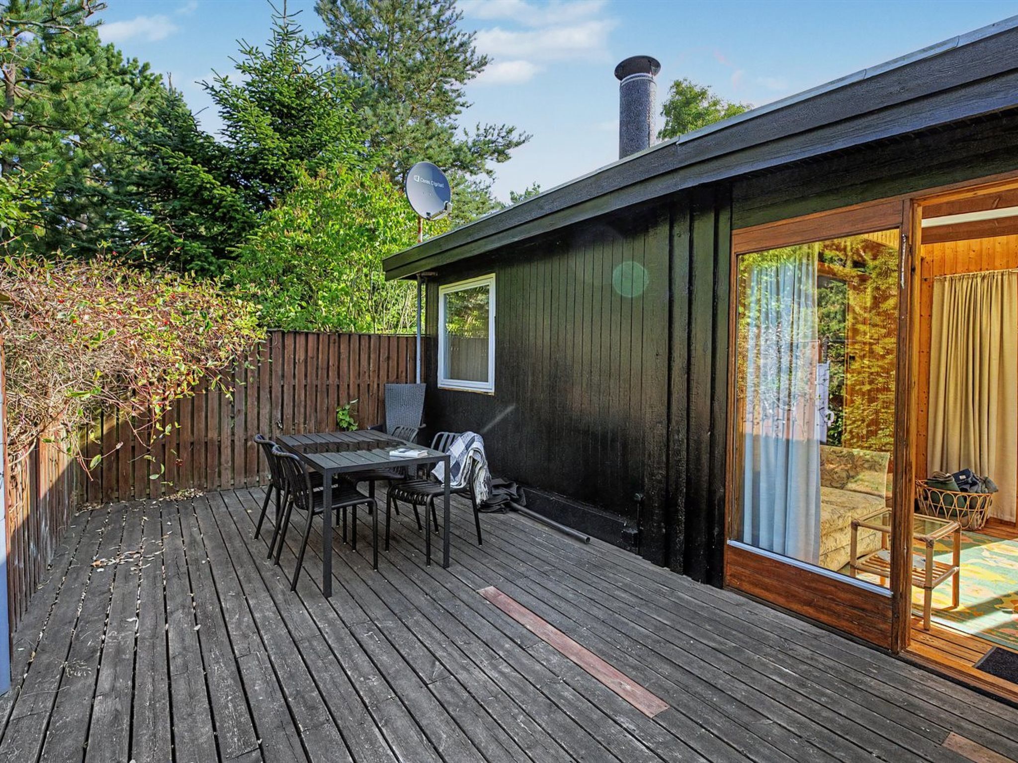 A wooden deck with a table and chairs, a satellite dish, and a sliding glass door leading to a room.