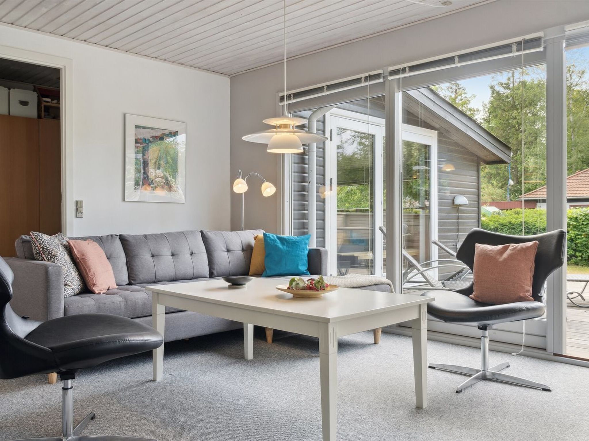 Un salon moderne avec un canapé gris, une table basse blanche et un fauteuil noir. Un tableau orne le mur et une fenêtre offre une vue sur l’extérieur.