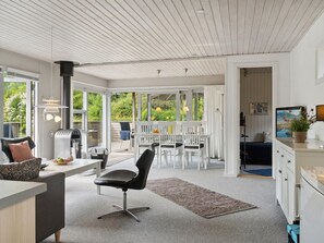 A modern kitchen with white cabinetry, a dining area with white chairs, and a large window overlooking a garden.