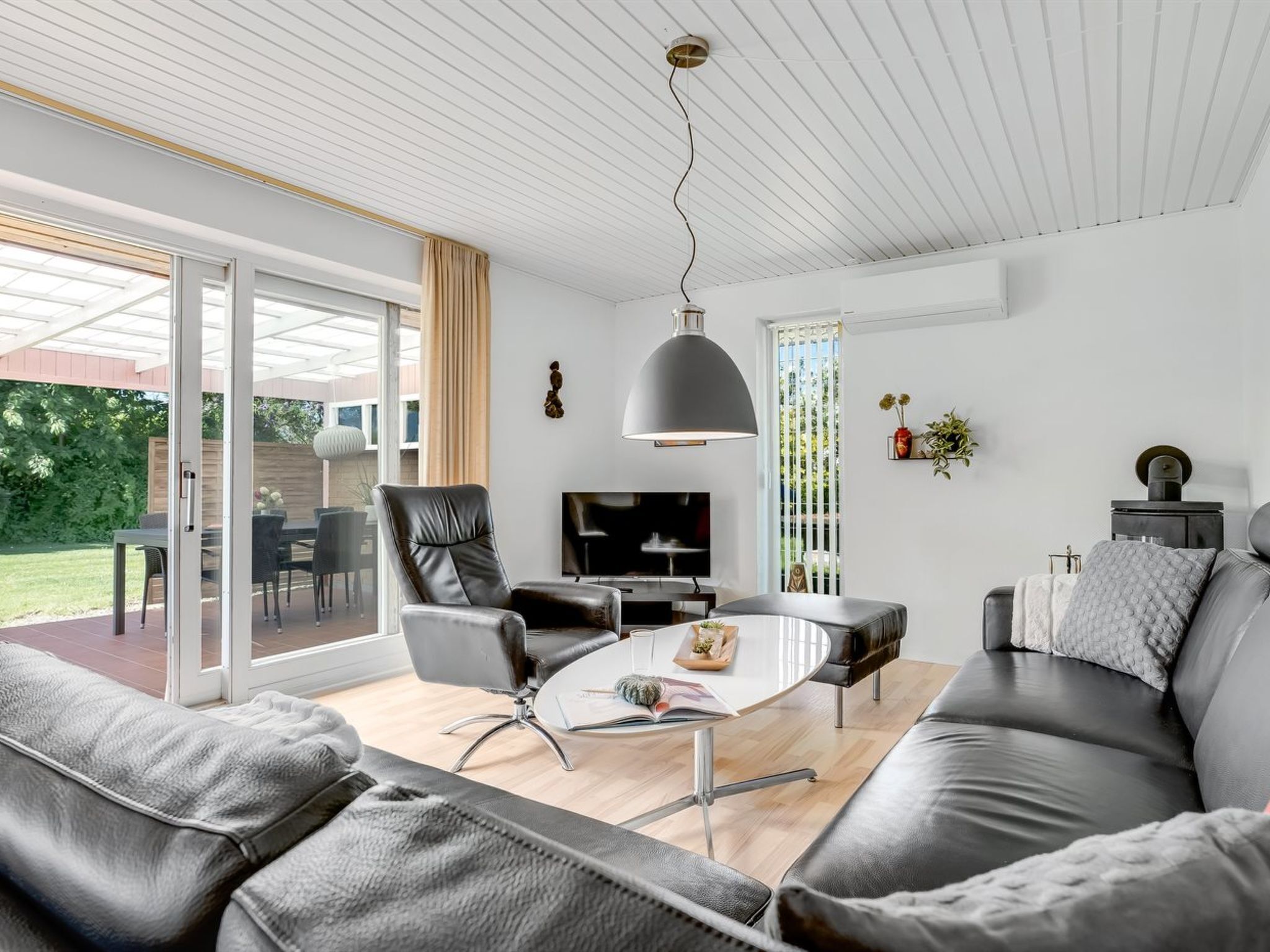 Un salon moderne avec un canapé, une table à manger et un téléviseur. Une porte-fenêtre coulissante donne accès à un espace extérieur.