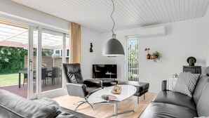 A modern living room with a sofa, a dining table, and a TV. There is a sliding glass door leading to an outdoor area. - "Maleen" - 150m to the fjord by Interhome (Nakskov)