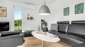A modern living room with a black leather sofa, a white coffee table, a black TV, and a large window with a view of greenery. - "Maleen" - 150m to the fjord by Interhome (Nakskov)