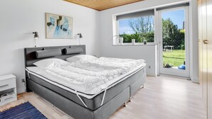 A modern bedroom with a large bed, a wooden ceiling, a window with a view of greenery, and a painting on the wall. - "Maleen" - 150m to the fjord by Interhome (Nakskov)