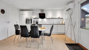 Une cuisine moderne avec des meubles blancs, un coin repas avec des chaises noires et une grande fenêtre donnant sur l’extérieur.