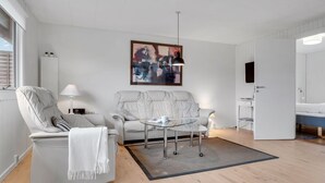 Un salon moderne avec un canapé, un fauteuil et une table basse. Un tableau est accroché au mur, et un téléviseur est fixé au mur.