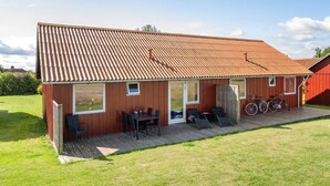 Une maison en bois avec un toit en tuiles, une terrasse avec des meubles d’extérieur et des vélos garés devant.