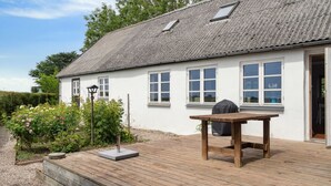 Ein weißes Haus mit geneigtem Dach, einer Holzterrasse und einem Grilltisch.