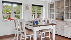 Ein Essbereich mit Holztisch und Stühlen, einer Vitrine mit Glastüren und Fenstern mit Blick auf Grünflächen.