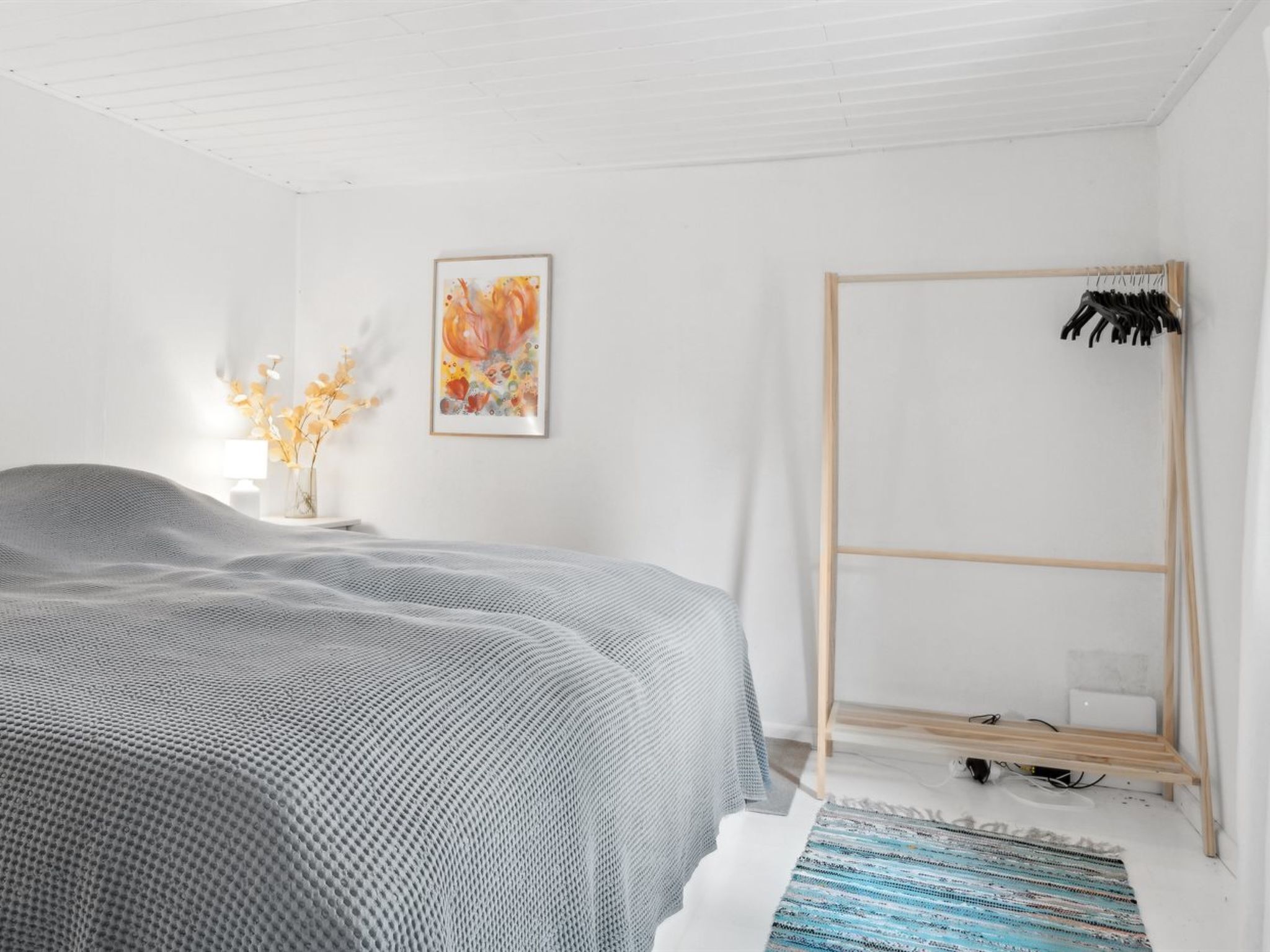 Ein modernes Schlafzimmer mit einem großen Bett, einem Holzschrank, einem Gemälde und einer Blumenvase.