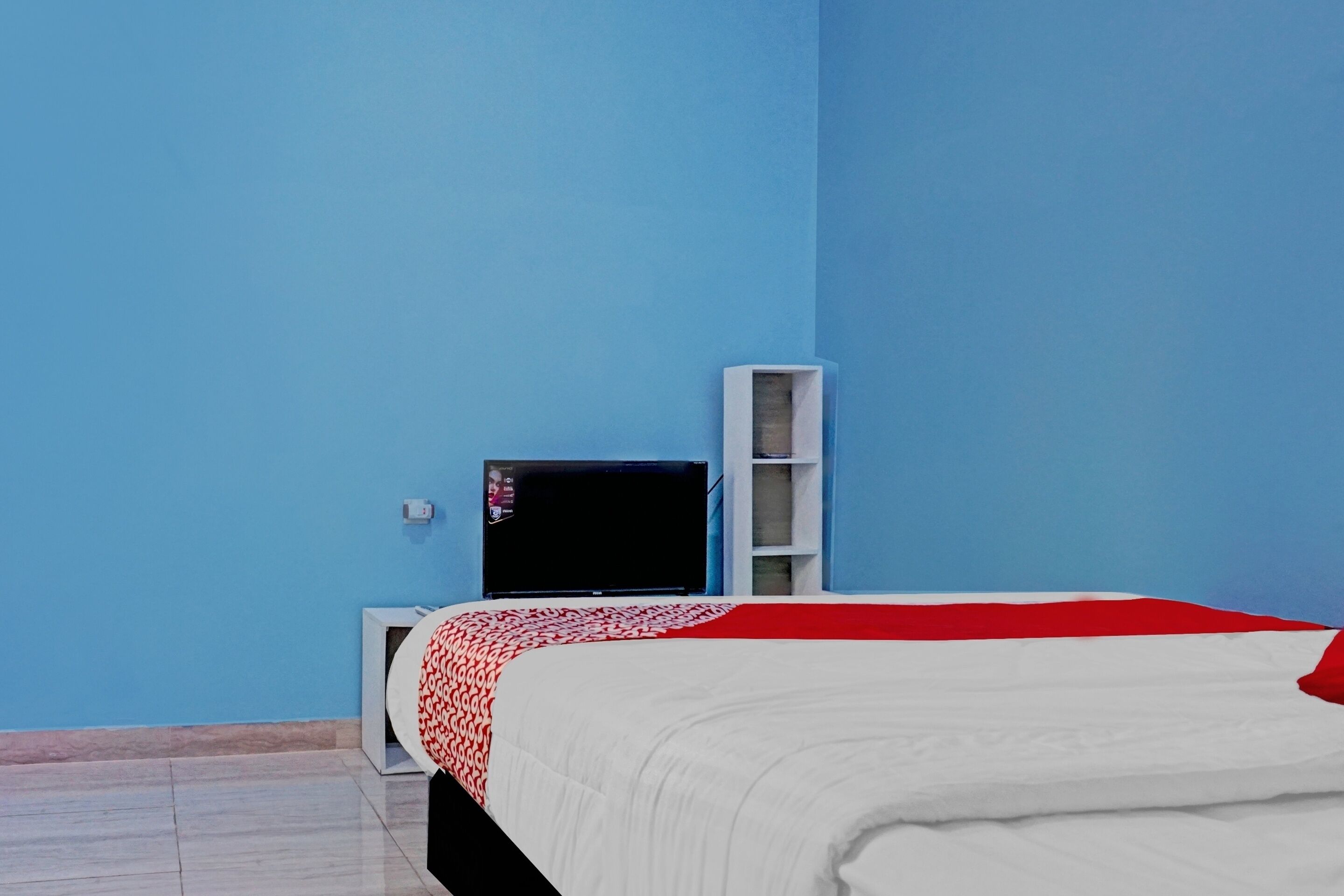 Una habitación con una cama, un televisor y un estante blanco sobre una pared azul.