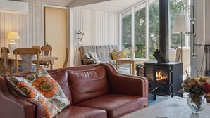 Ein gemütliches Wohnzimmer mit Ledersofa, Esstisch mit Stühlen, Kamin und großen Fenstern mit Blick ins Freie.