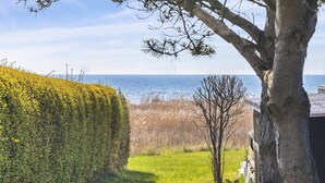 Ein angelegter Garten mit Hecke, einer Rasenfläche und Blick auf das Meer mit Windkraftanlagen in der Ferne.