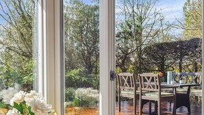 Eine Holzterrasse mit Tisch und Stühlen, umgeben von Bäumen und einem Garten.