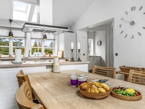 Uma cozinha moderna com mesa de madeira posta para o café da manhã, com croissants, frutas e xícaras de café.