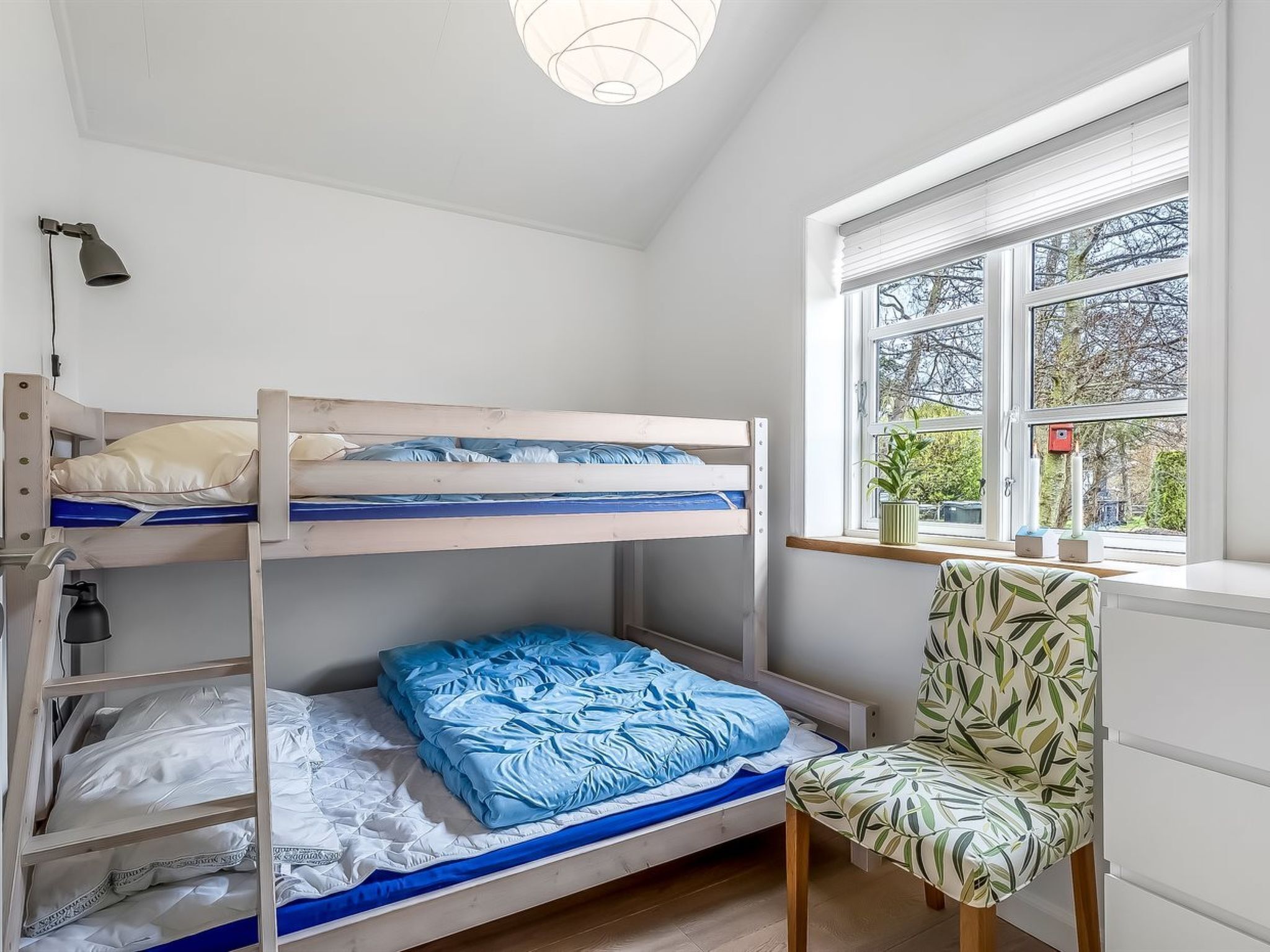 A bunk bed room with a window, a chair, and a desk.