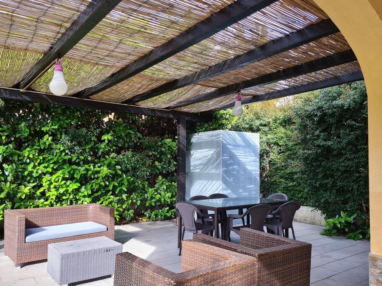 An outdoor patio with wicker furniture, a table, and a covered area with a mesh screen.