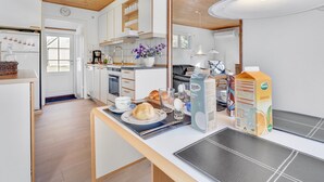 A modern kitchen with white cabinets, wooden ceiling, and a dining area with a table set for breakfast.