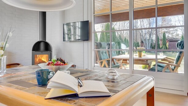 A modern kitchen with a wood-burning stove, a dining area with a table and chairs, and a large window providing a view of the outdoors.