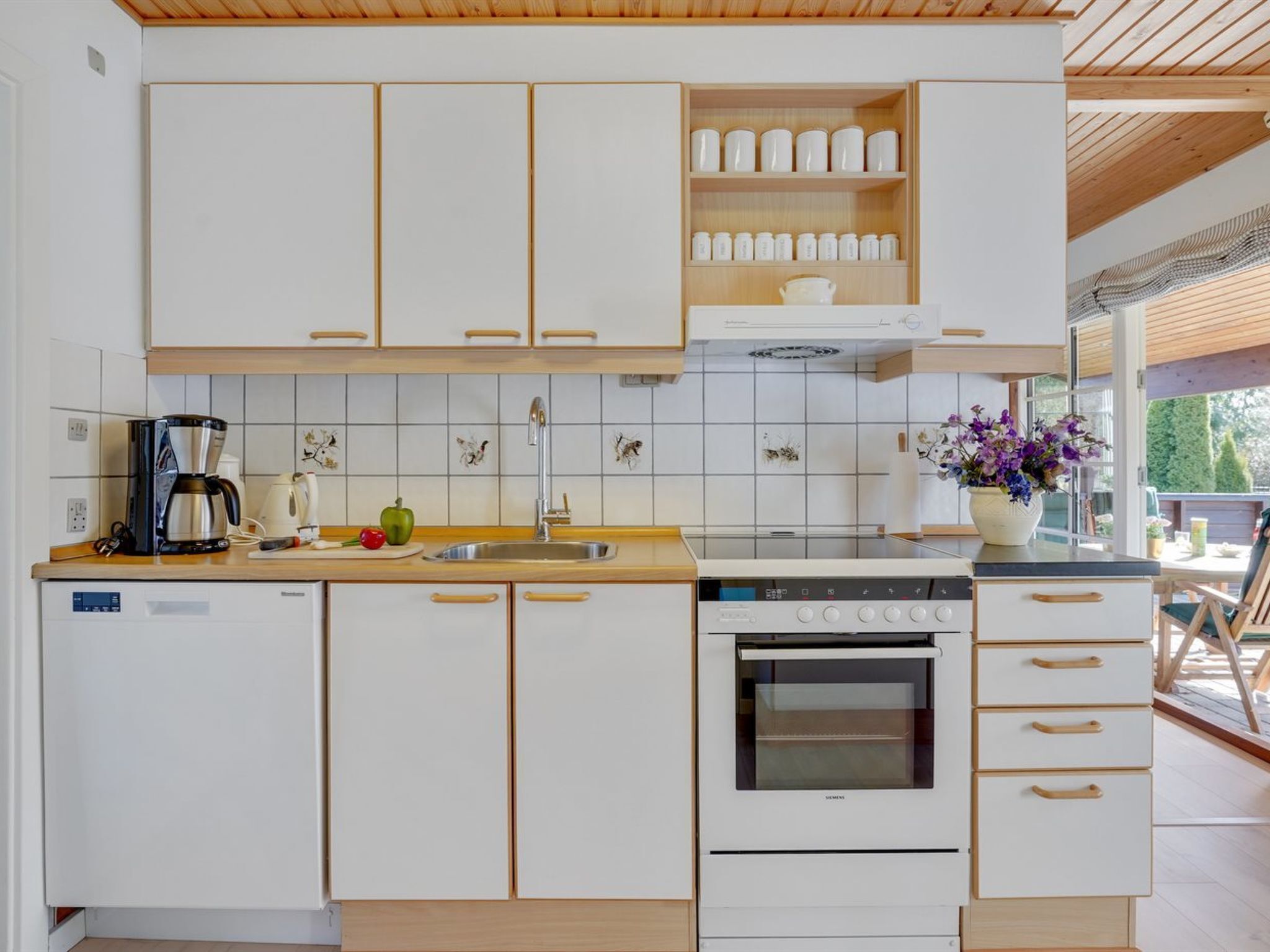 Een moderne keuken met witte kastjes, een roestvrijstalen koffiezetapparaat, een spoelbak en een fornuis.