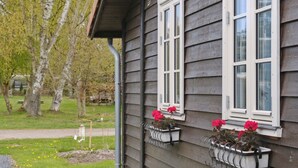 A house with a dark siding exterior, white window frames, and flower boxes with red flowers on the second floor.
