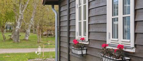 A house with a dark siding exterior, white window frames, and flower boxes with red flowers on the second floor.