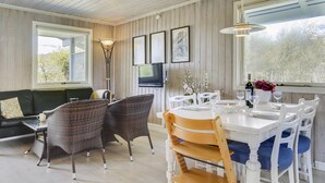 Un coin repas avec une table blanche dressée pour quatre personnes, entourée de chaises en osier et de chaises en bois avec des coussins bleus.