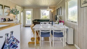 Un espace repas comprenant une table en bois, des chaises et un banc. Il y a également un coin cuisine avec un comptoir et un évier.