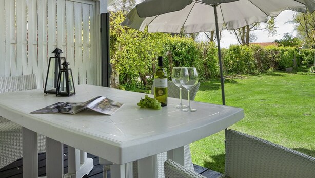 Une table de patio avec une bouteille de vin, deux verres et un magazine.