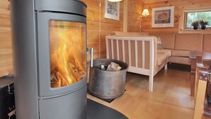 Ein Kaminofen in einer Holzhütte mit einer Couch und einem Fenster.