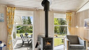 A cozy room with a wood-burning stove, large windows, and a comfortable seating area. - "Eini" - 500m from the sea by Interhome (Væggerløse)
