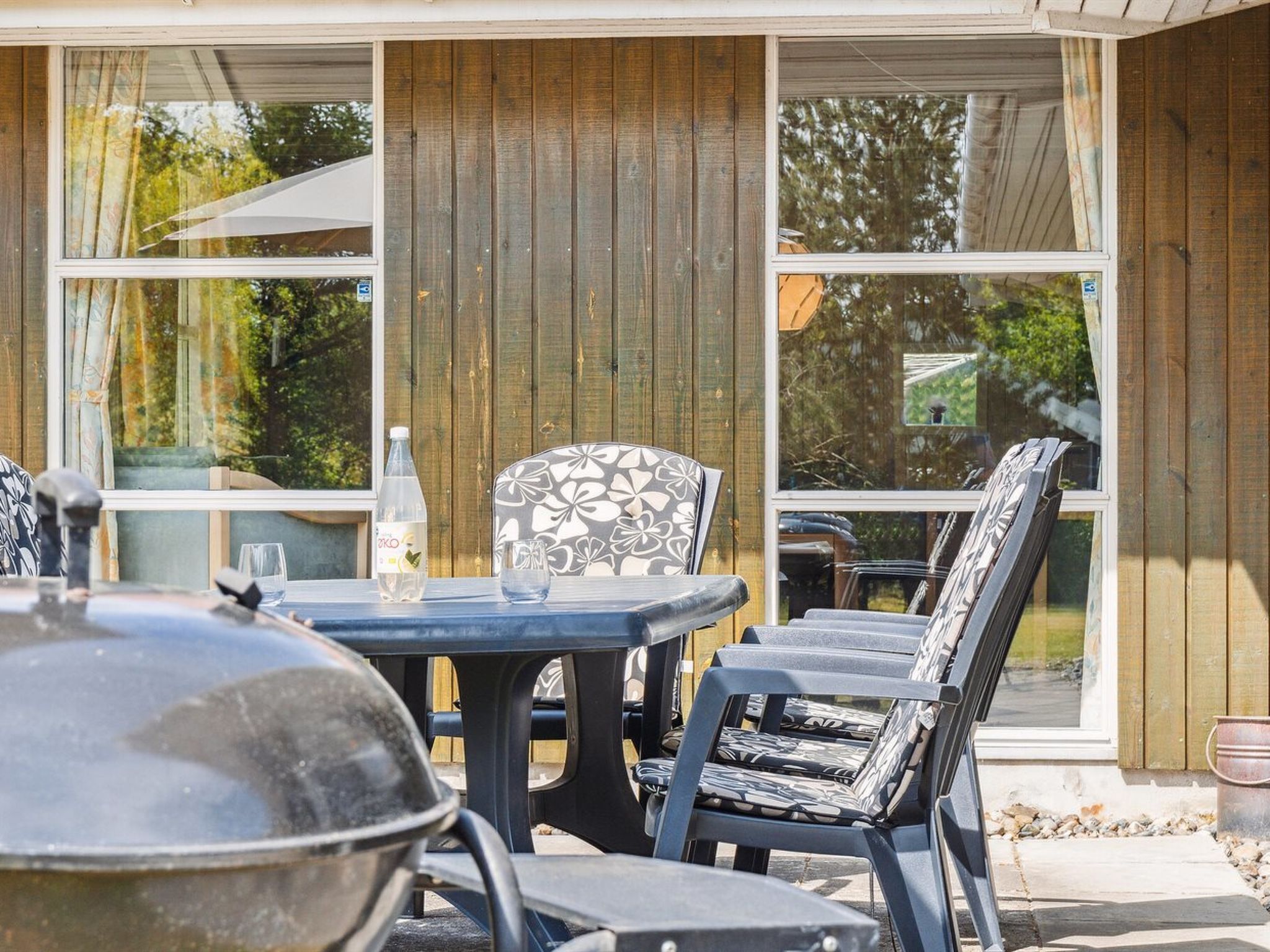 An outdoor patio with a table and chairs, a grill, and a bottle of water.