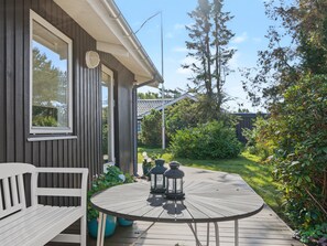 A wooden deck with a table and bench, surrounded by greenery and trees.