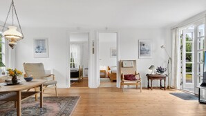 Une pièce spacieuse avec un plancher en bois, un coin repas comprenant une table et des chaises, un lit avec une tête de lit et une grande fenêtre avec des rideaux.