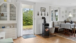 Une pièce chaleureuse avec un poêle à bois intégré, un coin repas avec une table et des chaises, un buffet blanc aux portes vitrées et une vue sur l’extérieur.