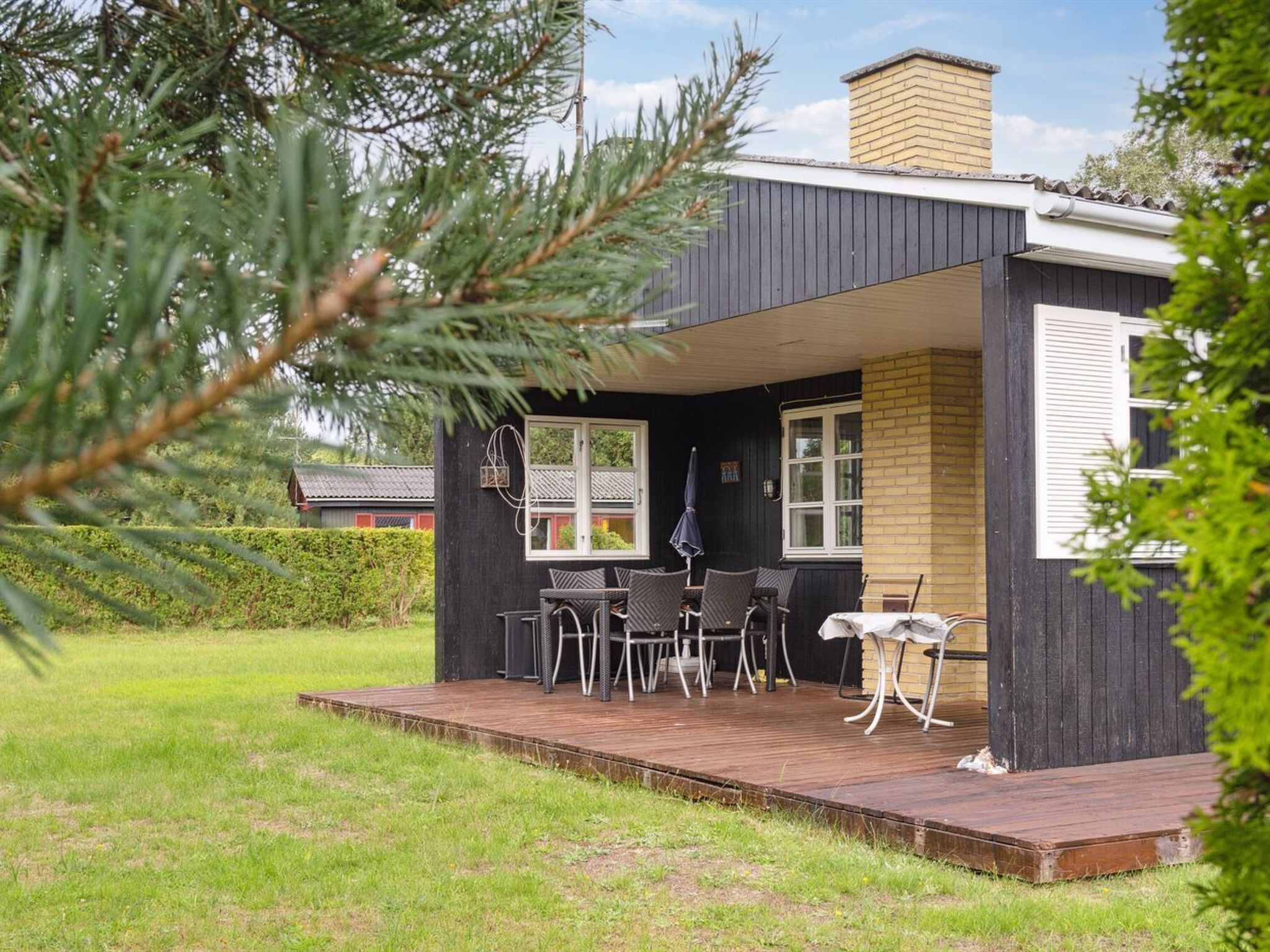 Une maison moderne dotée d’une terrasse en bois, d’un espace salon extérieur et d’un jardin bien entretenu.