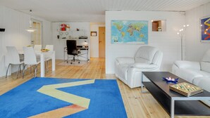 Un salón moderno con muebles blancos, un gran mapa mundial en la pared y una alfombra azul con diseño geométrico.