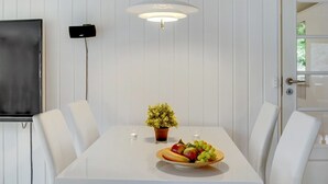 Comedor con una mesa blanca, sillas blancas, una planta en maceta y un frutero.