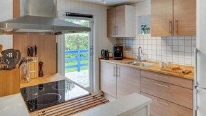 Cocina moderna con estufa integrada, armarios de madera, campana extractora de acero inoxidable y vistas al exterior.